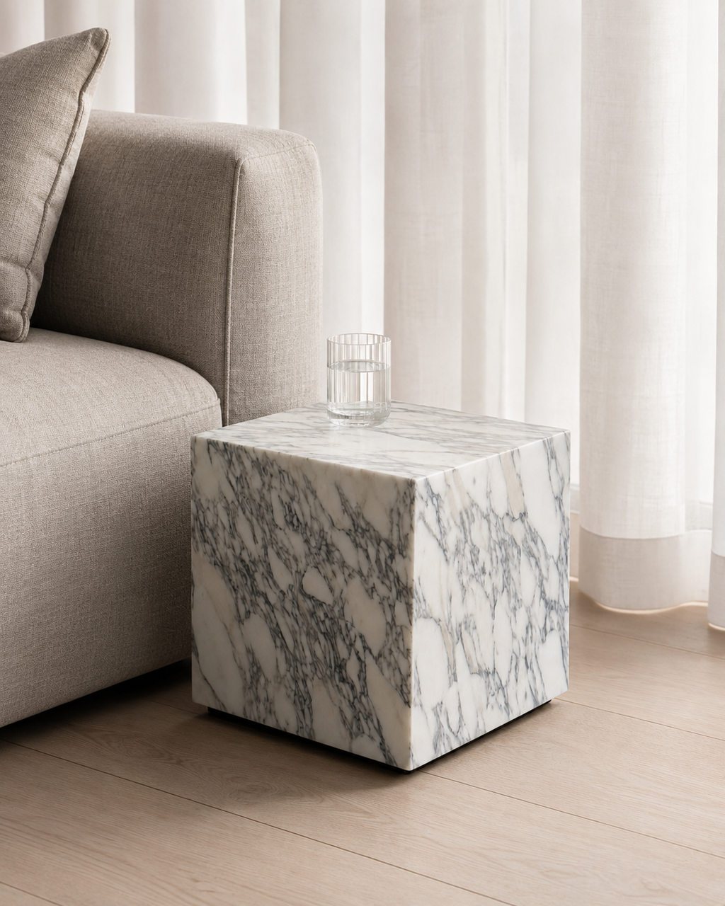 Luxury white marble cube with grey veining pattern placed next to a beige linen sofa with curtains in living room.