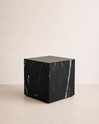 Luxury black marble with delicate white veining pattern cube side table in a off white studio background. Side view.