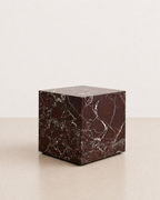 Luxury deep burgundy marble with delicate white veining pattern cube side table in a off white studio background. Side view.