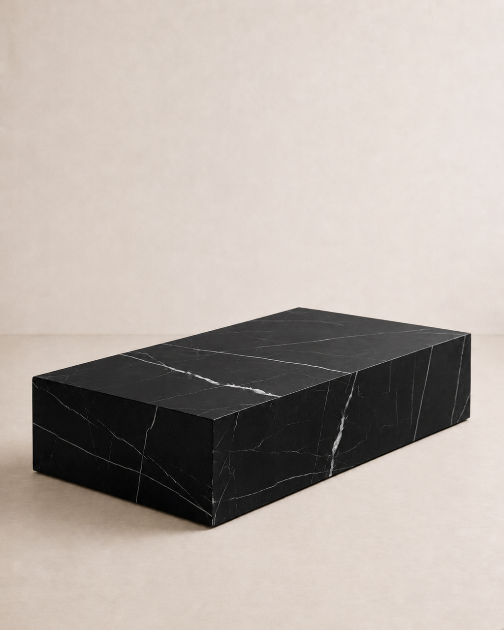 A minimal rectangular block coffee table, with black marble and delicate white veining in an off-white studio. Angled view. 