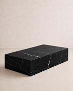 A minimal rectangular block coffee table, with black marble and delicate white veining in an off-white studio. Angled view. 