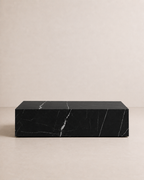 A minimal rectangular block coffee table, made of black marble and delicate white veining in an off-white studio. Front view. 
