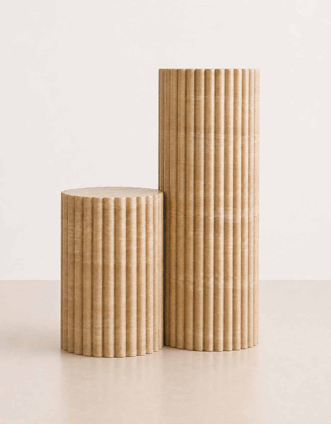 A pair of short and tall fluted beige travertine plinths with natural grain texture placed in a off white studio.