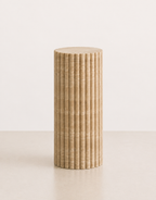 A medium fluted beige travertine plinth with natural grain texture placed in a beige studio. Front view.