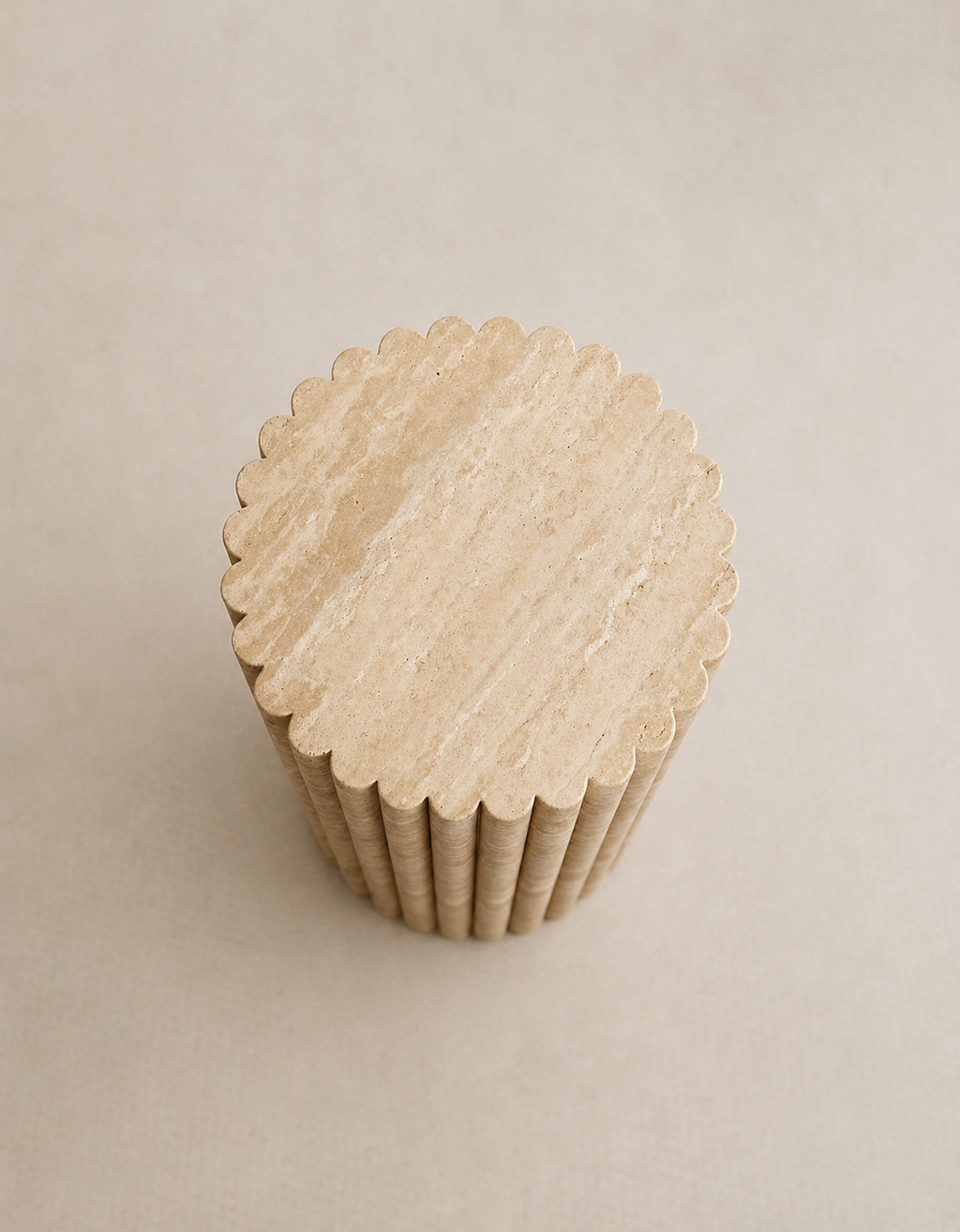 A tall fluted beige travertine plinth with natural grain texture placed in a beige studio. Top view.
