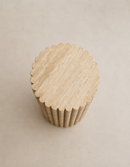 A tall fluted beige travertine plinth with natural grain texture placed in a beige studio. Top view.