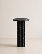 Black marble side table with a ribbed cylindrical design n a beige background