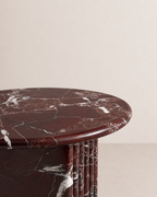 Close up of a luxury burgundy red marble side table with a ribbed cylindrical design in a beige background. Honed finishing.