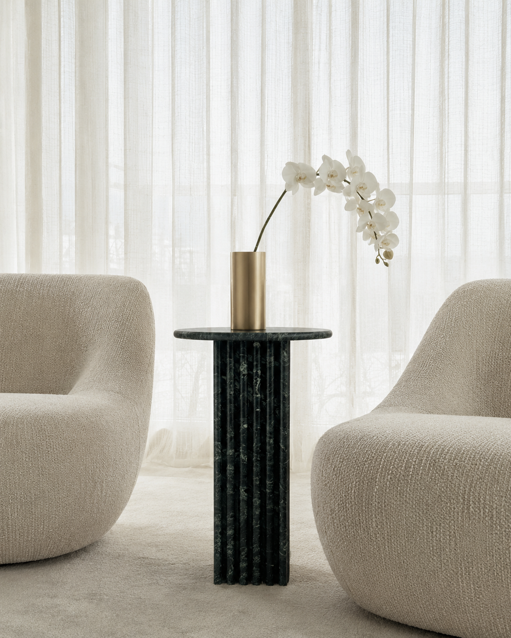 Deep emerald green marble side table with a ribbed cylindrical design, placed with a beige armchair and candle in a lounge room with curtains. Modern interior.