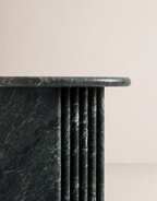 Close up of emerald green marble side table with a ribbed cylindrical design n a beige background