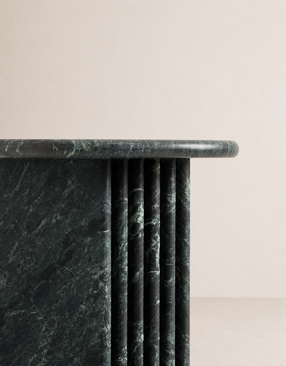Close up of emerald green marble side table with a ribbed cylindrical design n a beige background