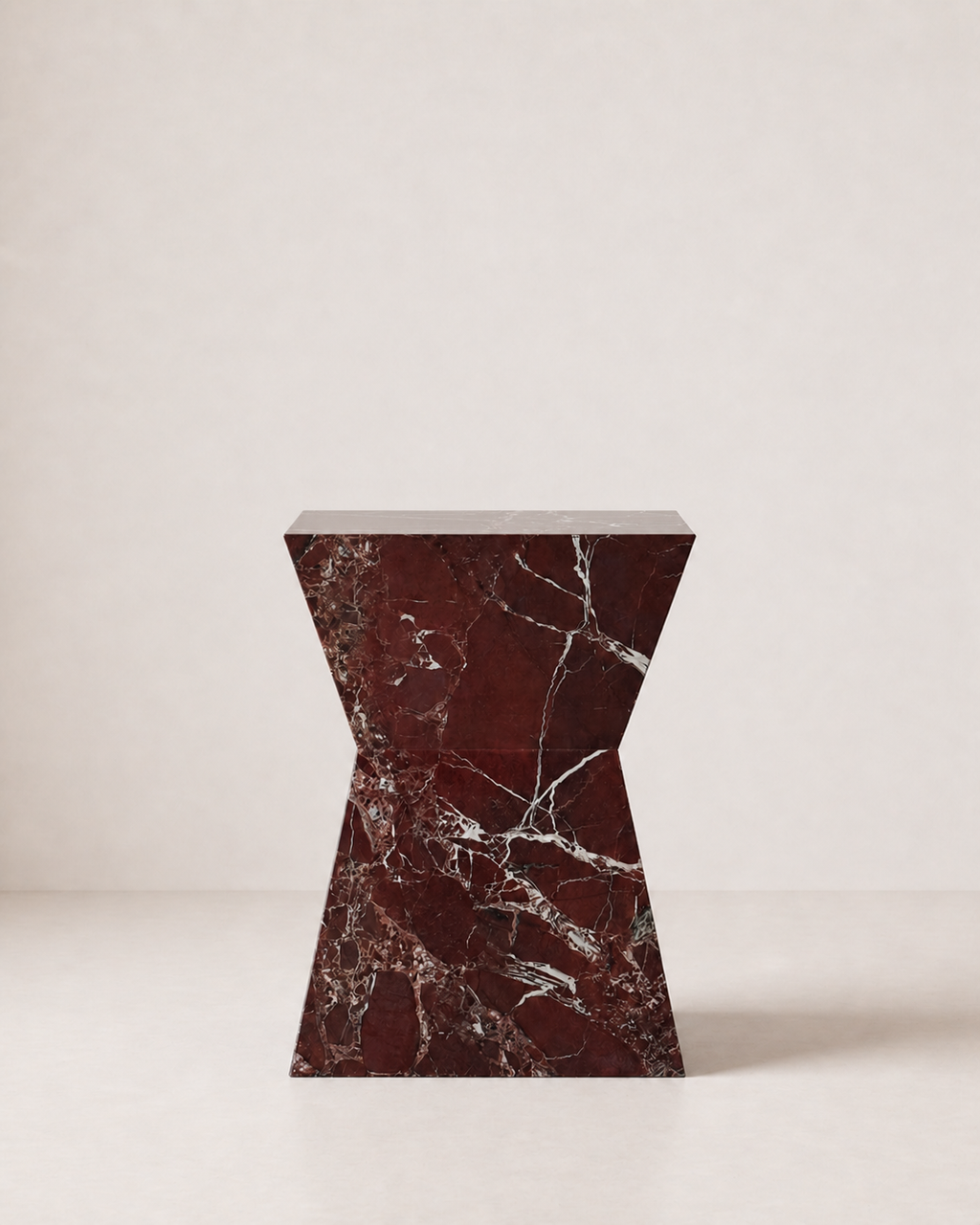 Hourglass shaped marble side table, made of luxury burgundy red marble with delicate white veining, placed in a light beige studio. Front view.