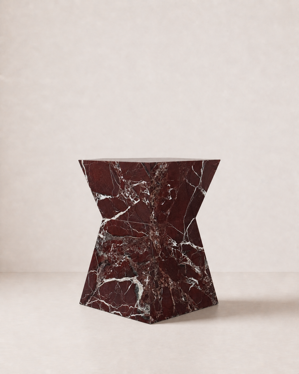 Hourglass shaped marble side table, made of luxury burgundy red marble with delicate white veining, placed in a light beige studio. Side view.