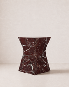 Hourglass shaped marble side table, made of luxury burgundy red marble with delicate white veining, placed in a light beige studio. Side view.