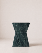 Hourglass shaped marble side table, made of luxury emerald green marble with delicate white veining, placed in a light beige studio. Front view.