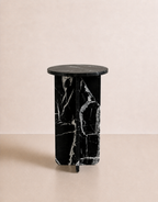 A luxury black marble with delicate white veining pattern round side table in a off white studio background. Front view.