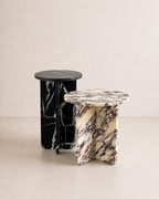 A set of two luxury black marble with delicate white veining pattern round side table in a off white studio background. Front view.